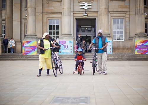 Woman, child and man with bikes outside Huddersfield Train Station