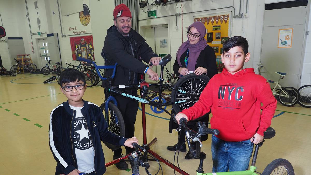 2 children and 2 adults with bikes in school hall