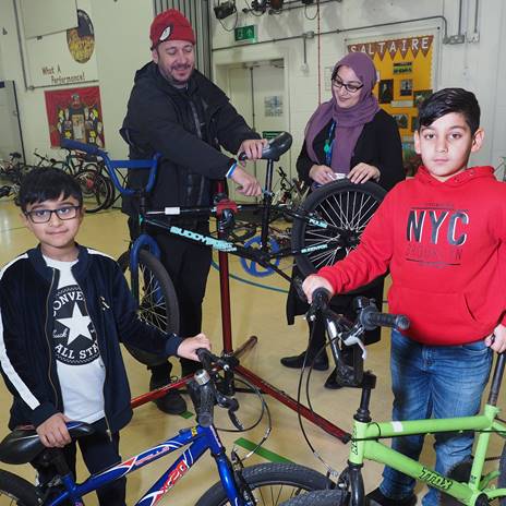 2 children and 2 adults with bikes in school hall