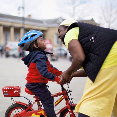 Small child on a bike and woman holding handlebars